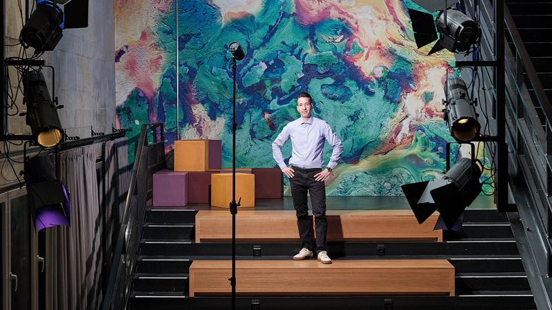 Picture of Nicolas Zanotti standing in a presentation hall with stage lights shining on him